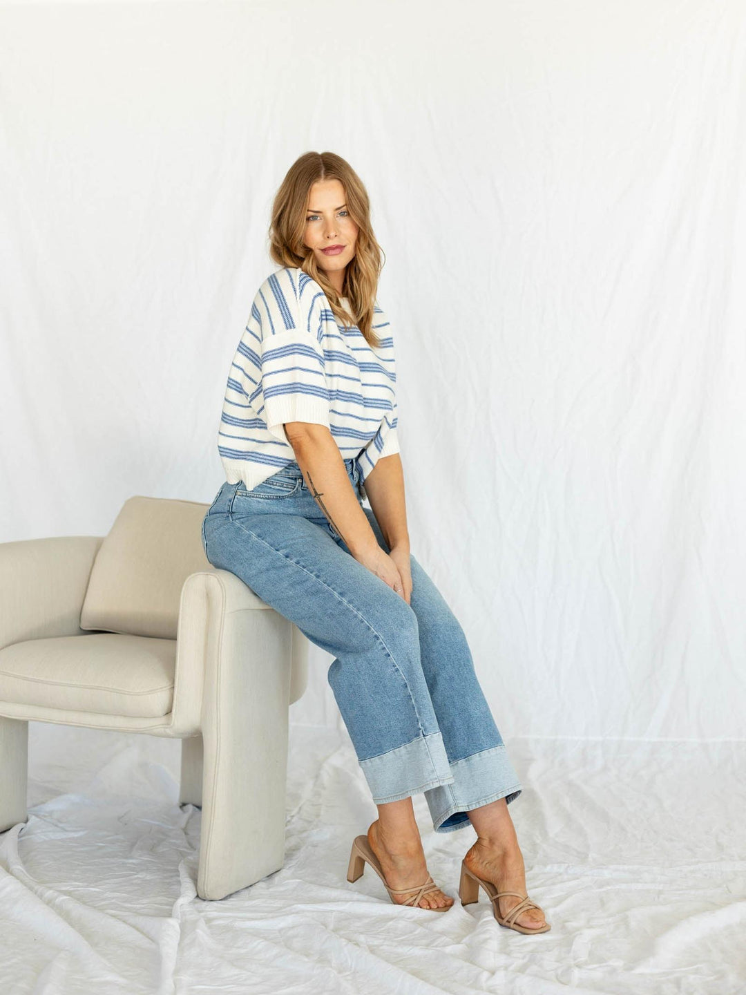Woman sitting on a chair wearing a striped shirt and jeans against a white background
