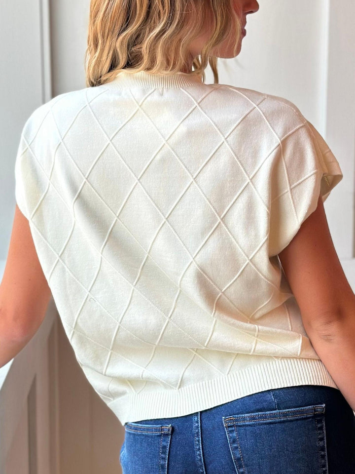 A woman shown from the back wearing a cream-colored short-sleeve knit sweater with a diamond argyle pattern and blue jeans.
