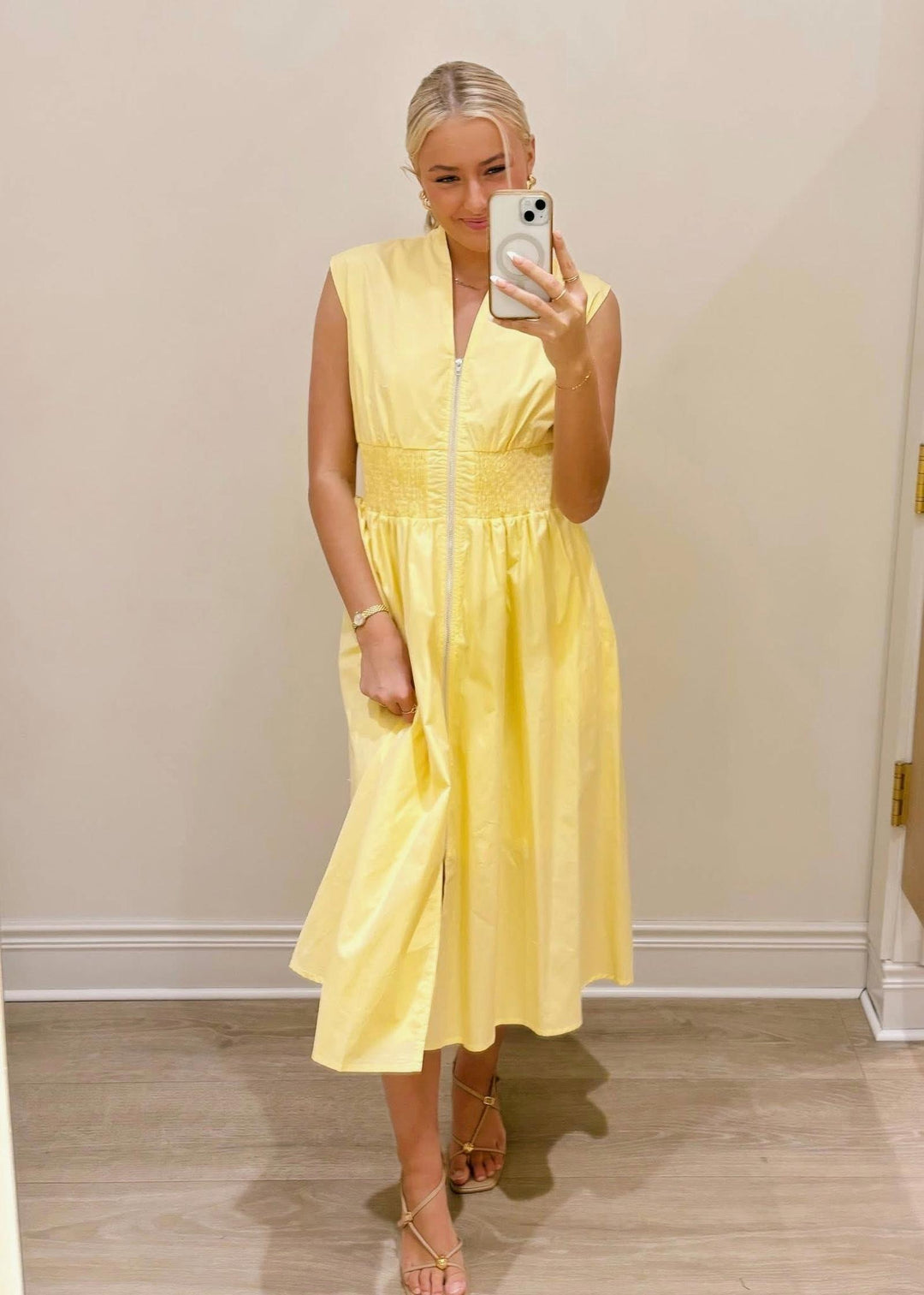 Woman wearing a yellow dress taking a mirror selfie.