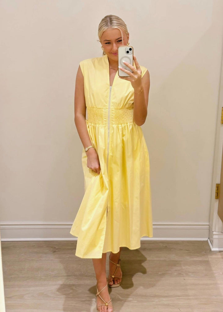 Woman wearing a yellow dress taking a mirror selfie.