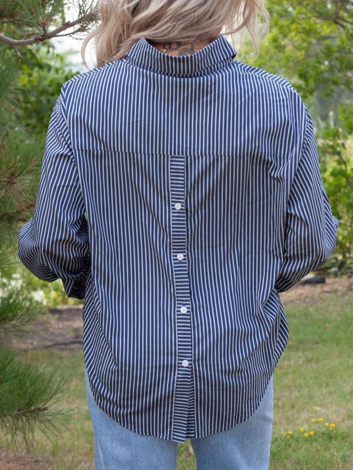 A person viewed from behind wearing a navy and white vertically striped button-down shirt and light blue jeans in an outdoor garden setting.