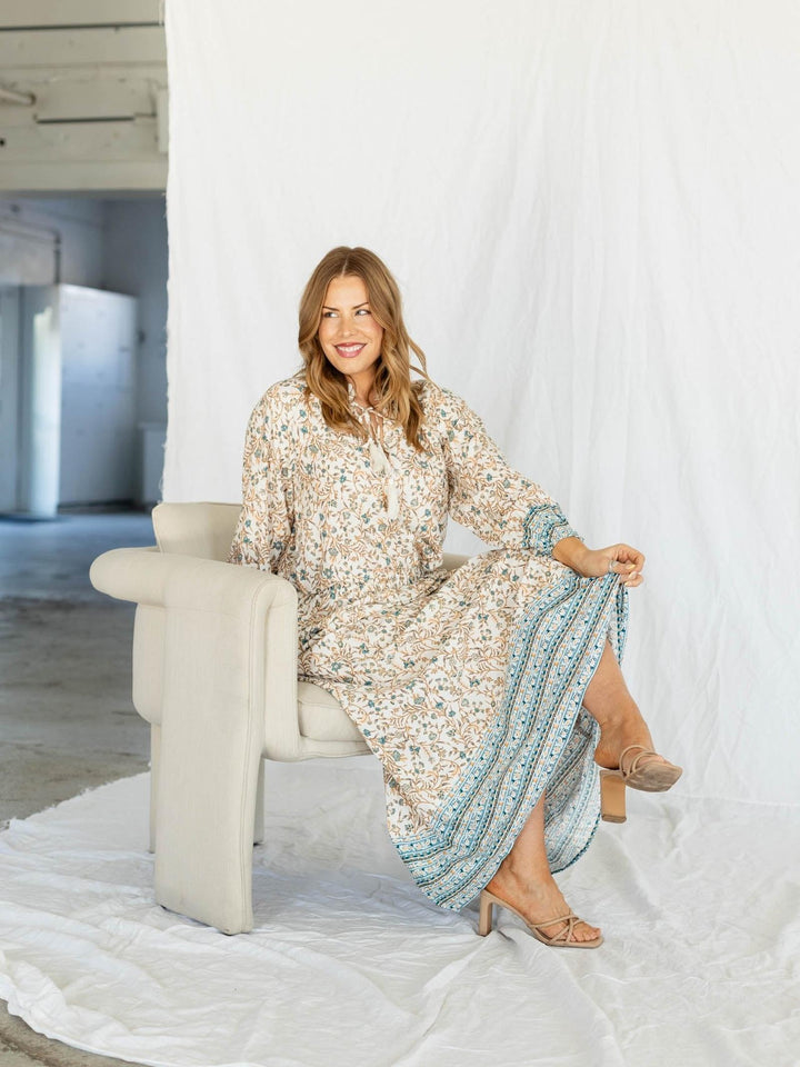 Woman in a floral dress sitting on a chair in a minimalistic room.