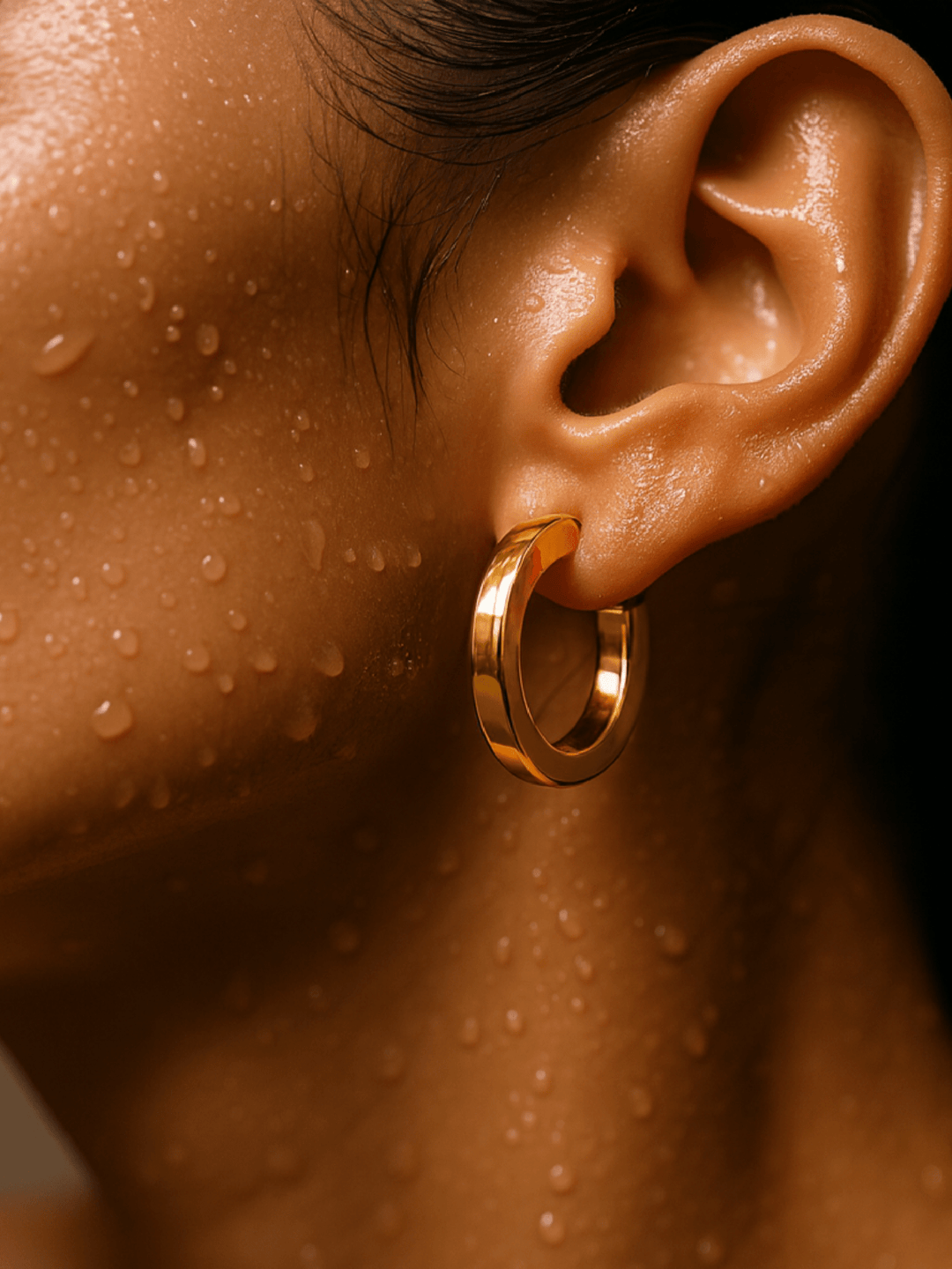 Close-up of an ear with a gold hoop earring on a wet skin background