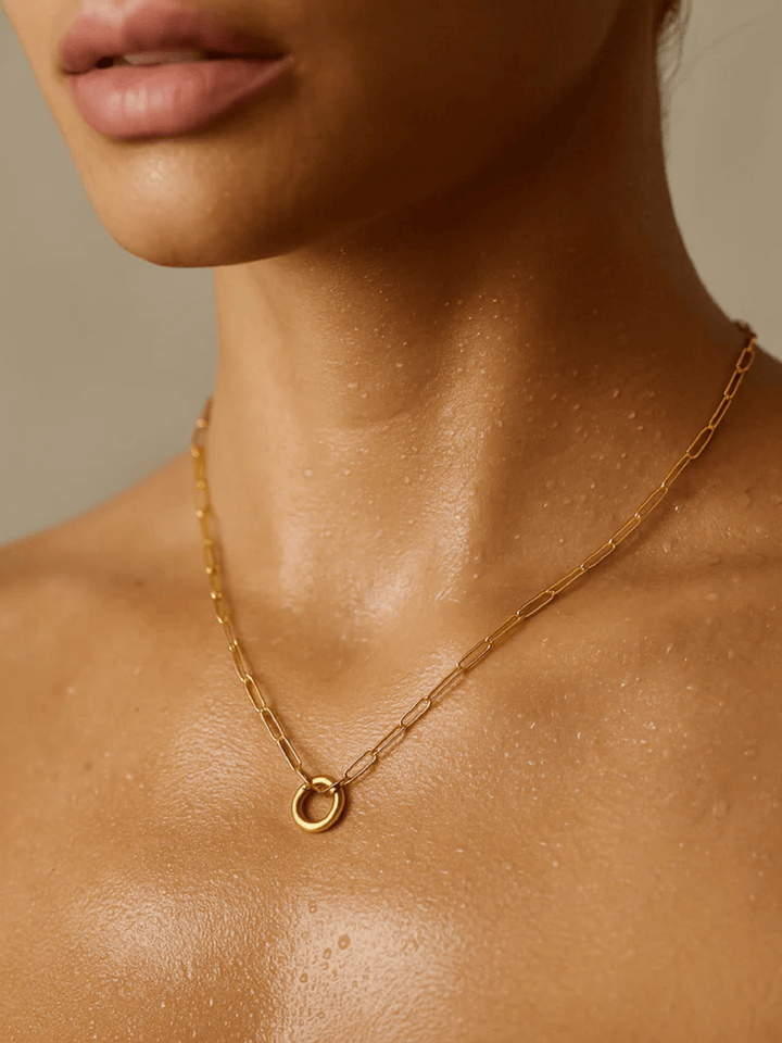 Close-up of a person wearing a gold necklace with a small round pendant on a neutral background