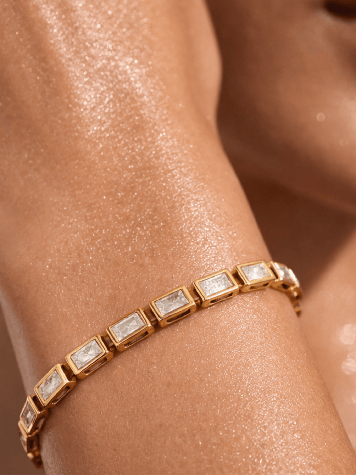 Gold bracelet with clear stones on a wrist against a neutral background