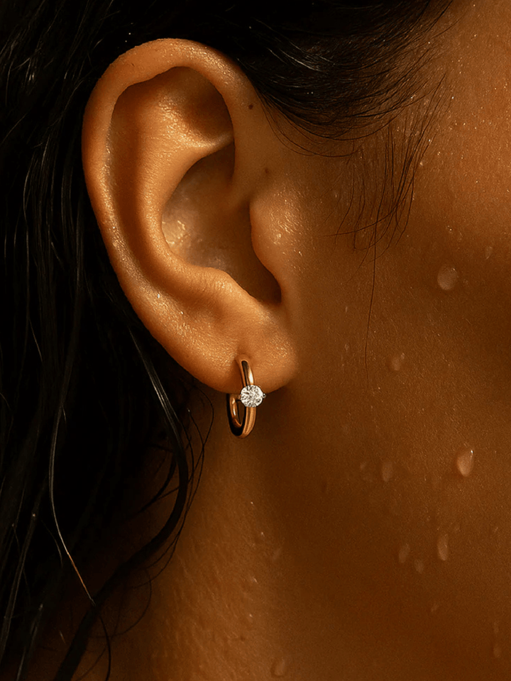 Close-up of an ear wearing a gold hoop earring with a diamond.