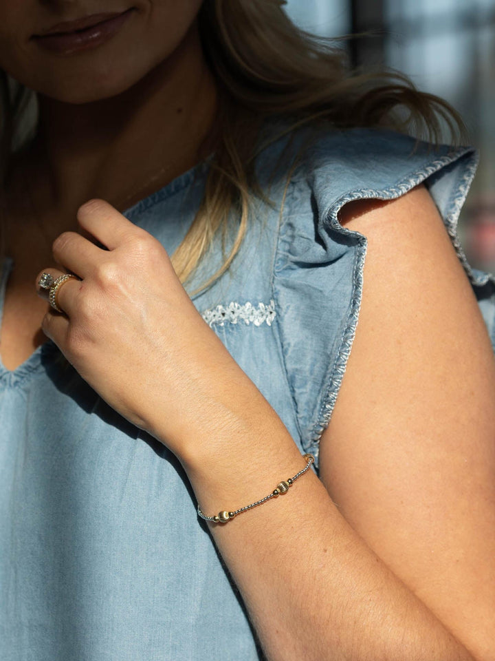 Close-up of a person wearing a light blue denim shirt with floral details and a bracelet.
