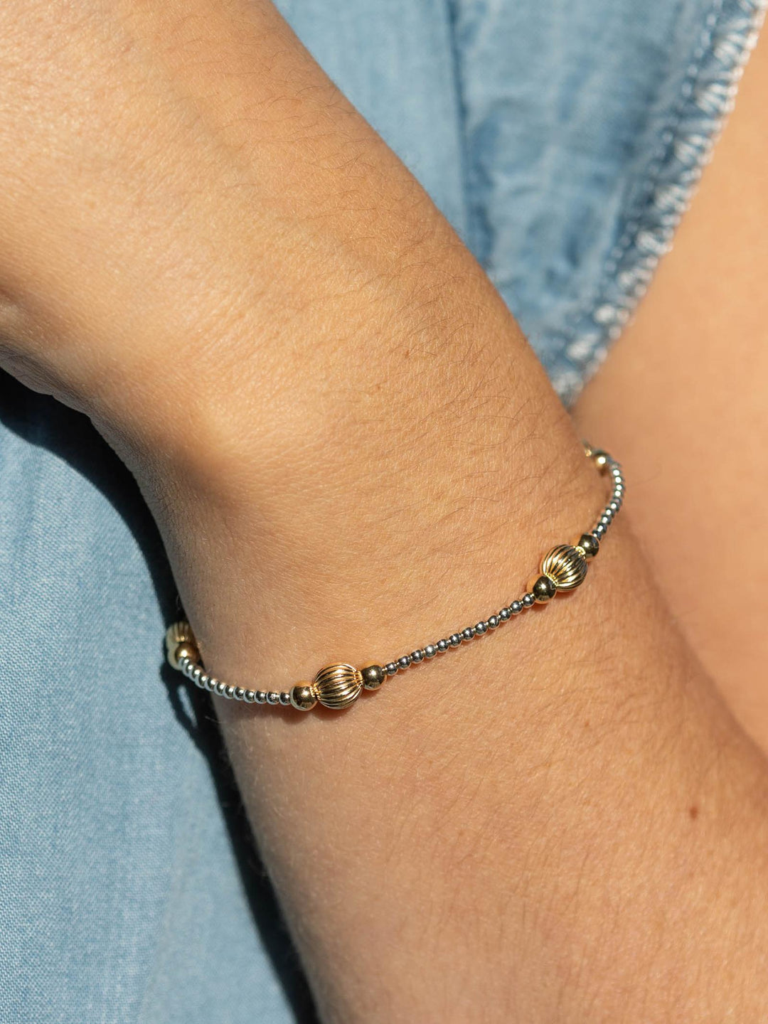 Gold beaded bracelet on a wrist with a denim background