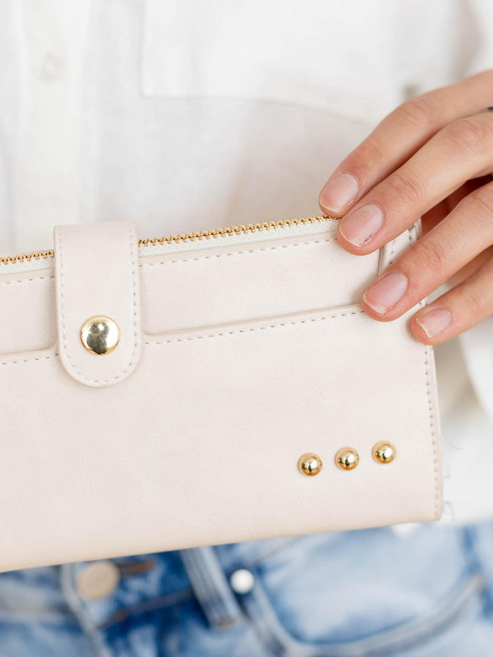Close-up of a hand holding a white wallet with gold accents.