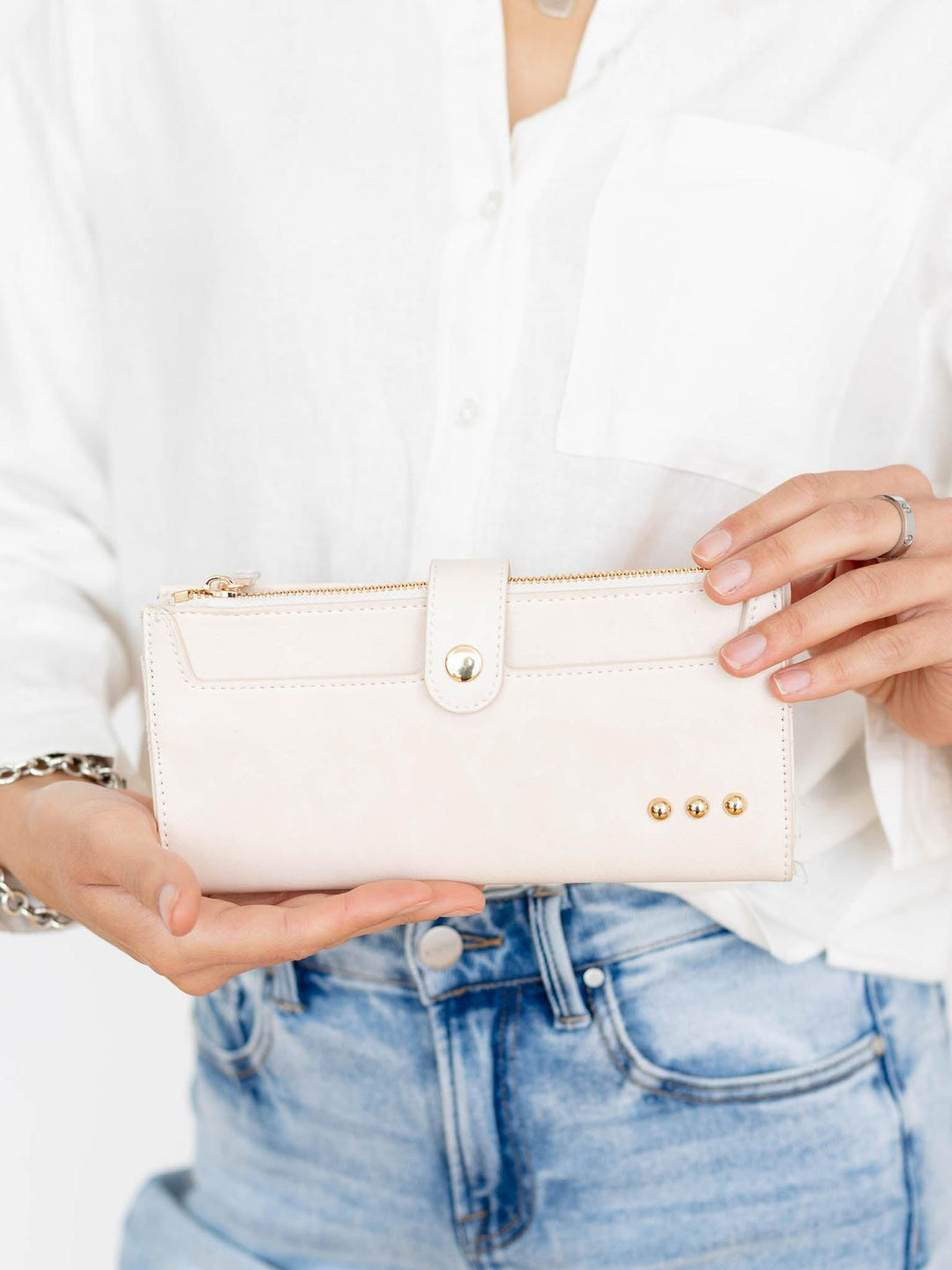 Person holding a white wallet with gold accents, wearing a white shirt and blue jeans.