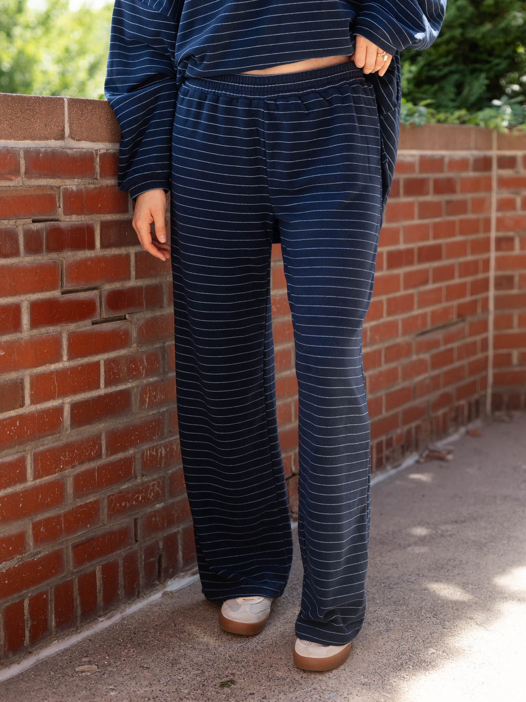A person wearing navy blue and white striped lounge pants and a matching top, standing outdoors against a red brick wall.