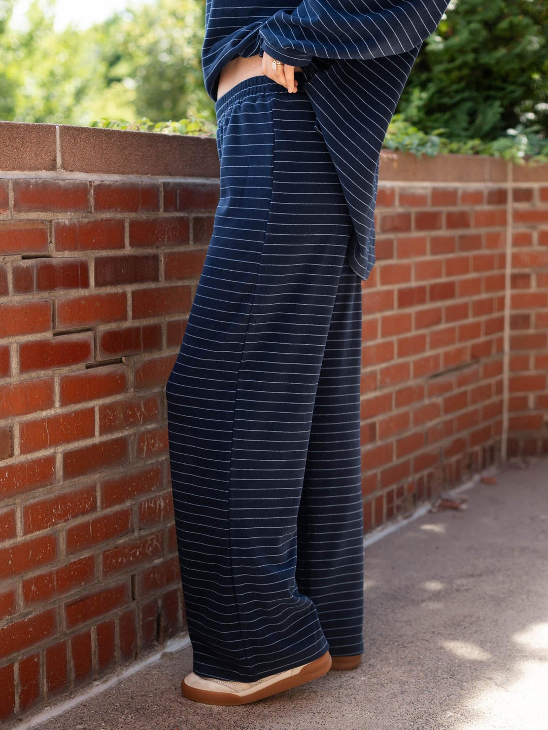 A person wearing navy blue wide-leg pants with thin white pinstripes, standing outdoors next to a red brick wall.