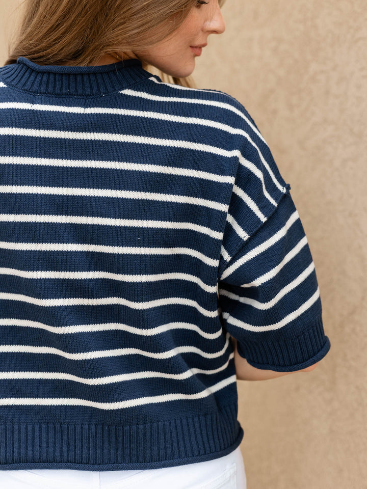 A woman wearing a navy blue and white horizontally striped knit sweater, shown from the back against a neutral beige textured wall.
