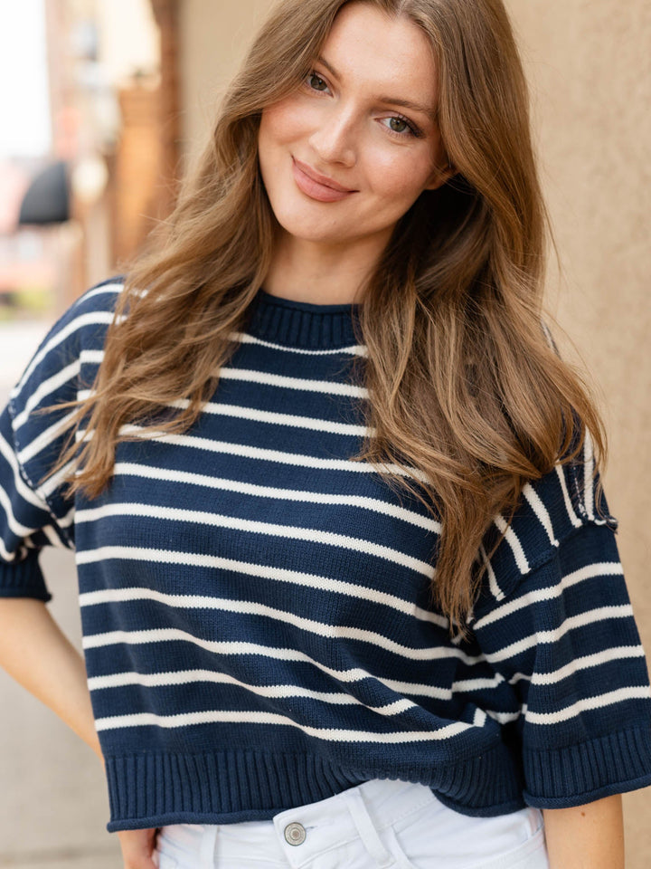 A woman wearing a navy blue and white horizontally striped knit sweater with short sleeves and a crew neck, paired with white pants.