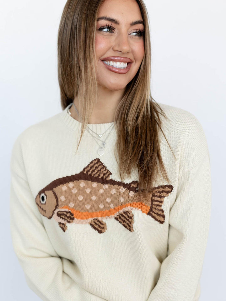 Woman wearing a cream sweater with a fish design on a plain background