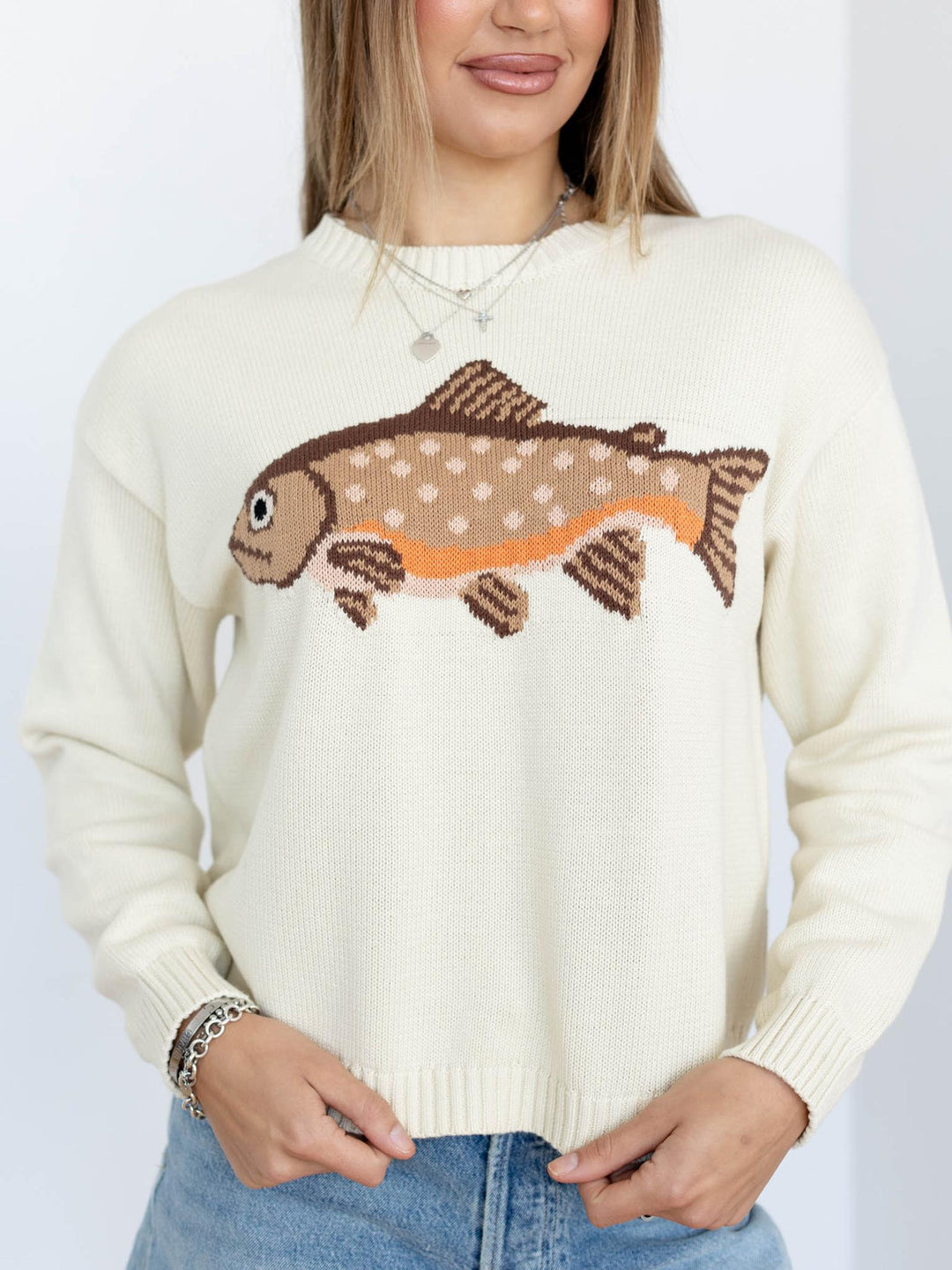Person wearing a cream sweater with a fish design on a plain background