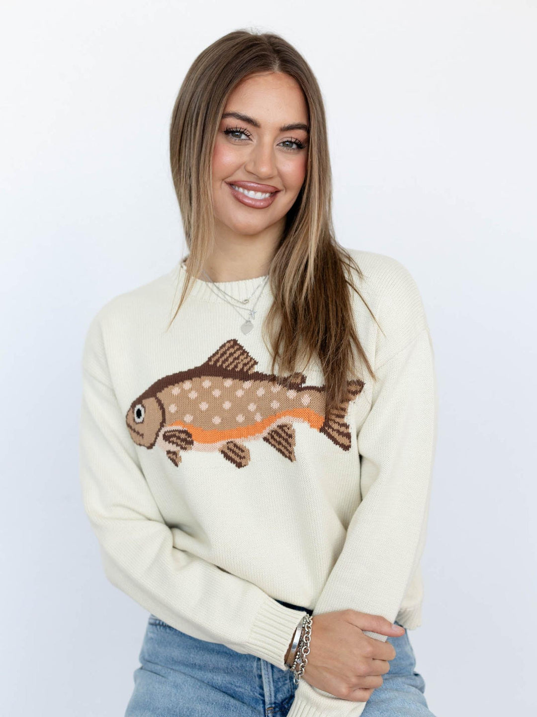 Woman wearing a cream sweater with a fish design on a white background