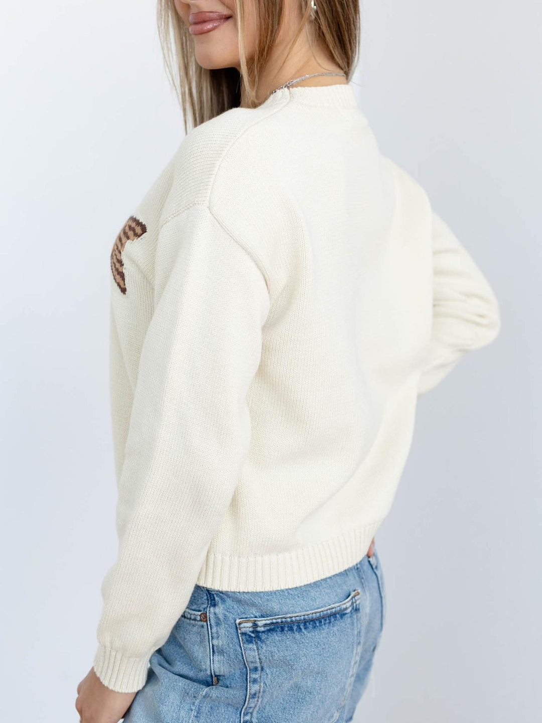 Person wearing a white sweater with a brown design on a plain background