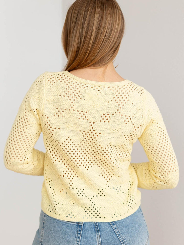 Woman wearing a light yellow crochet top with blue jeans on a plain background