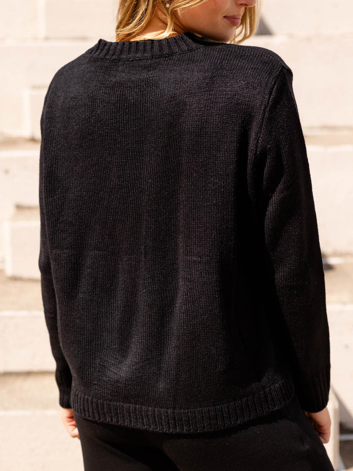 A person wearing a black ribbed knit sweater, shown from the back against a light stone wall.
