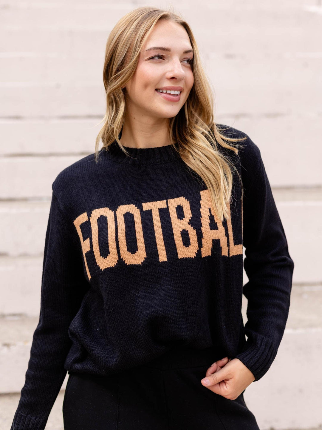 A woman wearing a black knit crewneck sweater with the word &