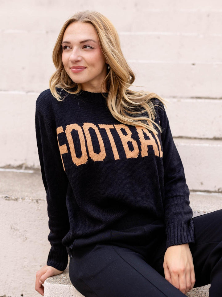 A woman sitting outdoors on concrete steps wearing a dark navy knit sweater with the word &