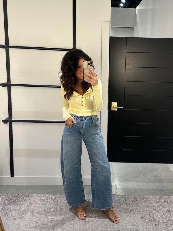 Person taking a mirror selfie wearing a yellow top and blue jeans in a room with a black door and ladder.