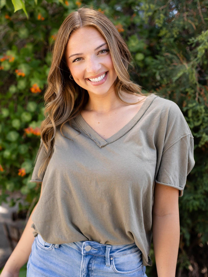 Smiling woman in an oversized olive green Free People Nina V-Neck Tee with rolled hem and reverse seams.