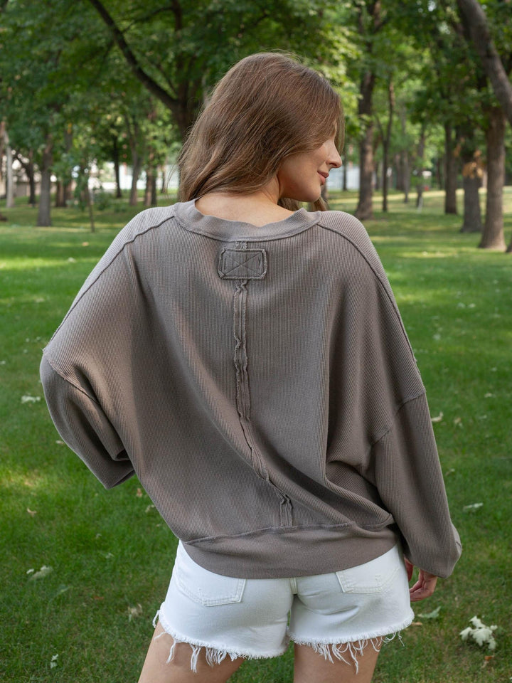A woman wearing a taupe-brown oversized sweatshirt and white denim shorts, photographed from behind in a park with green grass and trees.