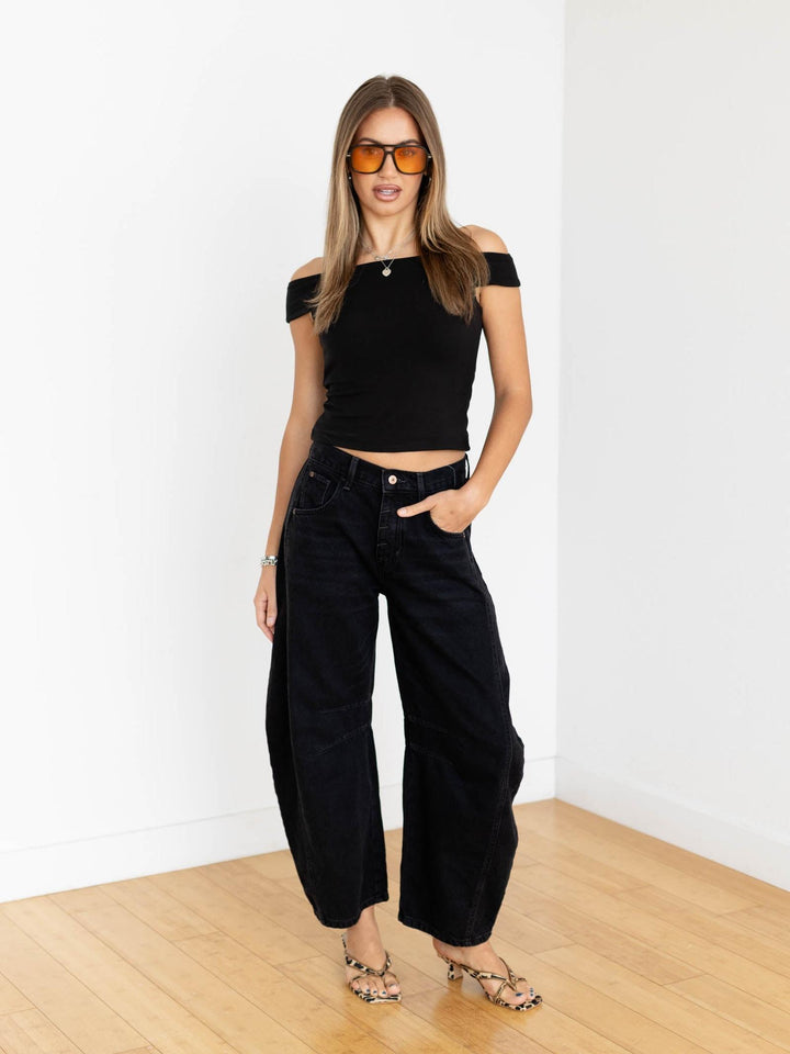 Woman wearing a black outfit with sunglasses in a minimalistic room.