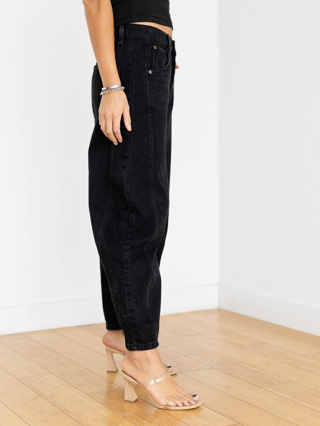 Person wearing black jeans on a wooden floor with a white wall background