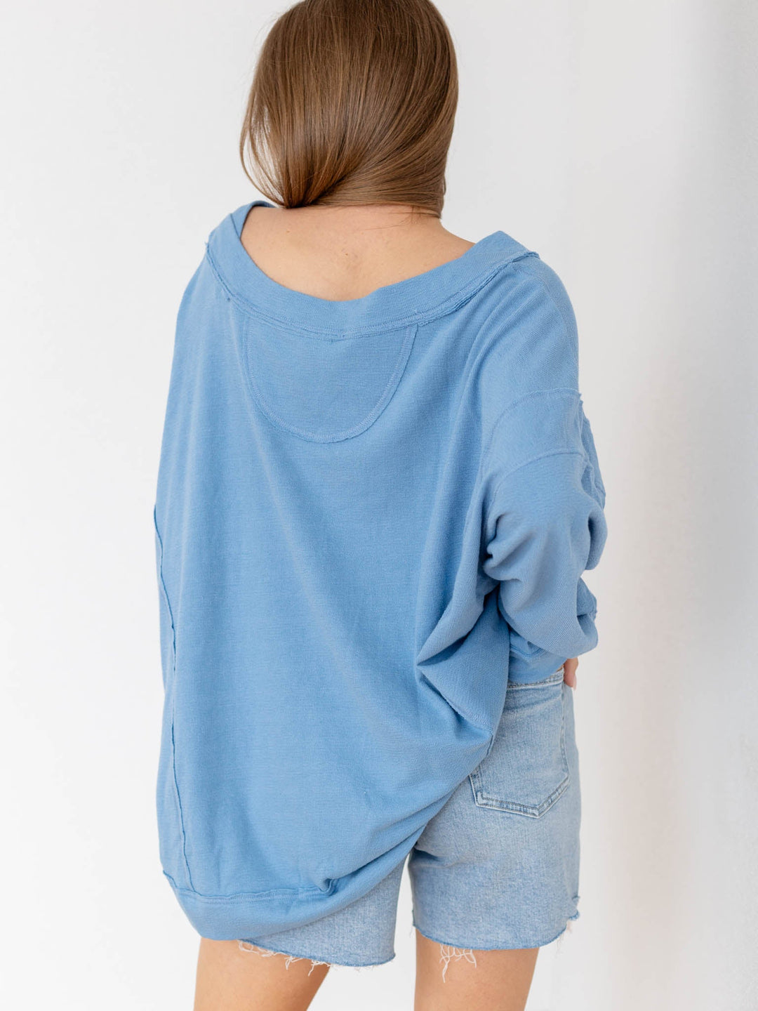 Woman wearing a blue oversized sweater and denim shorts against a white background