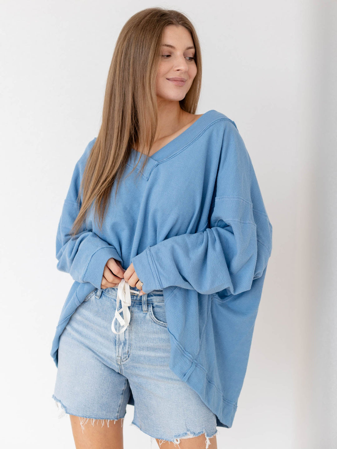Woman wearing a blue oversized sweater and denim shorts against a white background