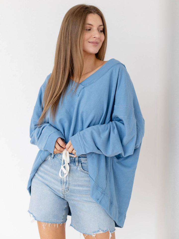 Woman wearing a blue oversized sweater and denim shorts against a white background