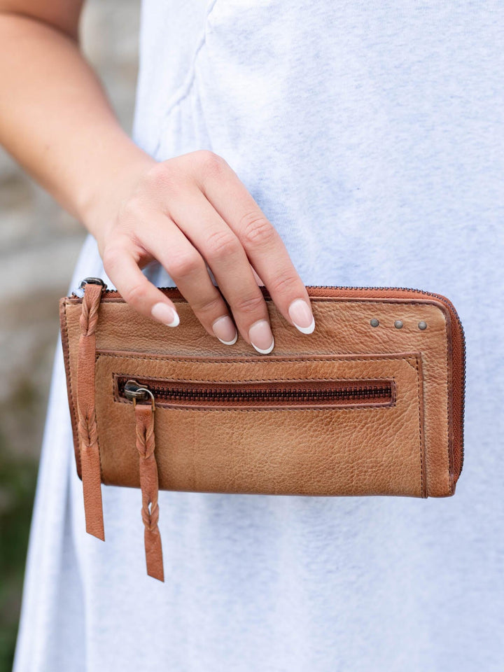 Hand holding a buttery-soft, warm Saddle Free People Emerson leather wallet with a front zip pocket and braided pull.