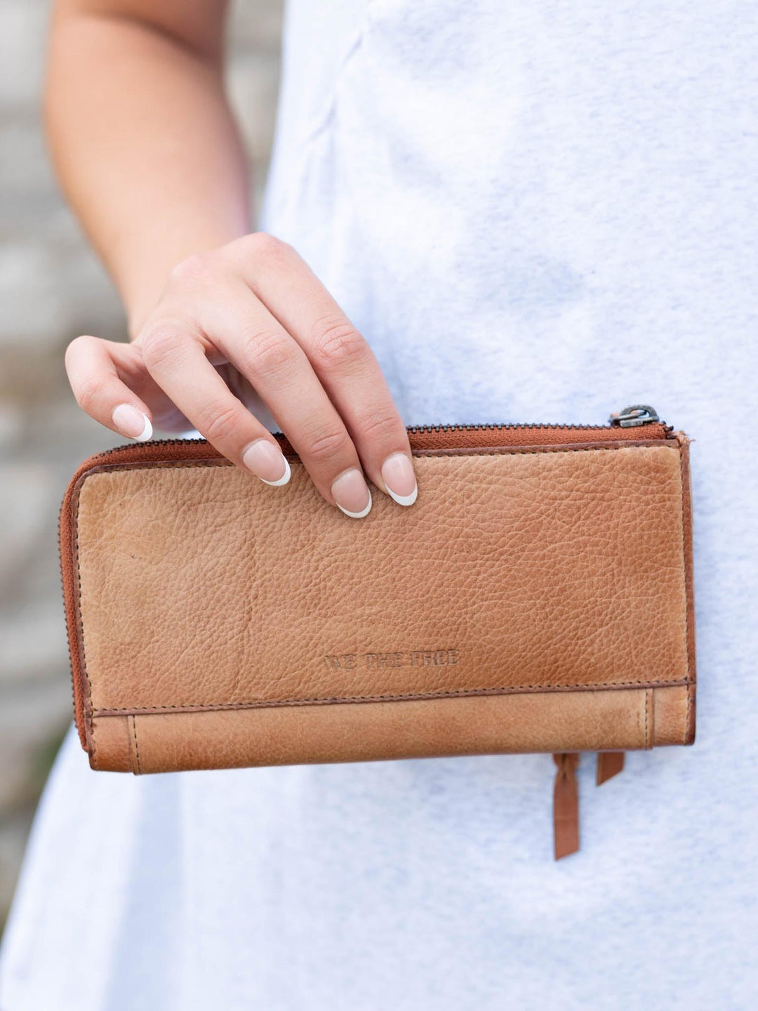 Hand holding a buttery-soft Saddle leather Free People Emerson Wallet with a zipper closure.