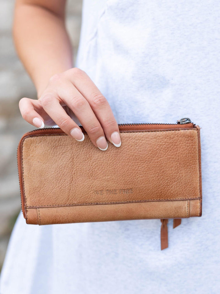 Hand holding a buttery-soft Saddle leather Free People Emerson Wallet with a zipper closure.