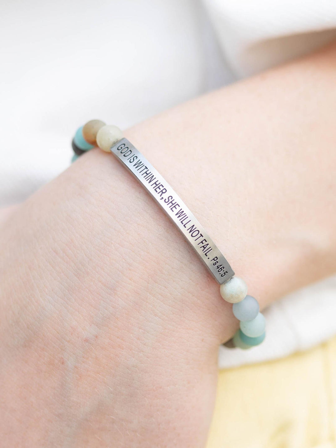 Hand wearing a stone bracelet with "GOD IS WITHIN HER, SHE WILL NOT FAIL. Ps 46:5" on a silver bar.