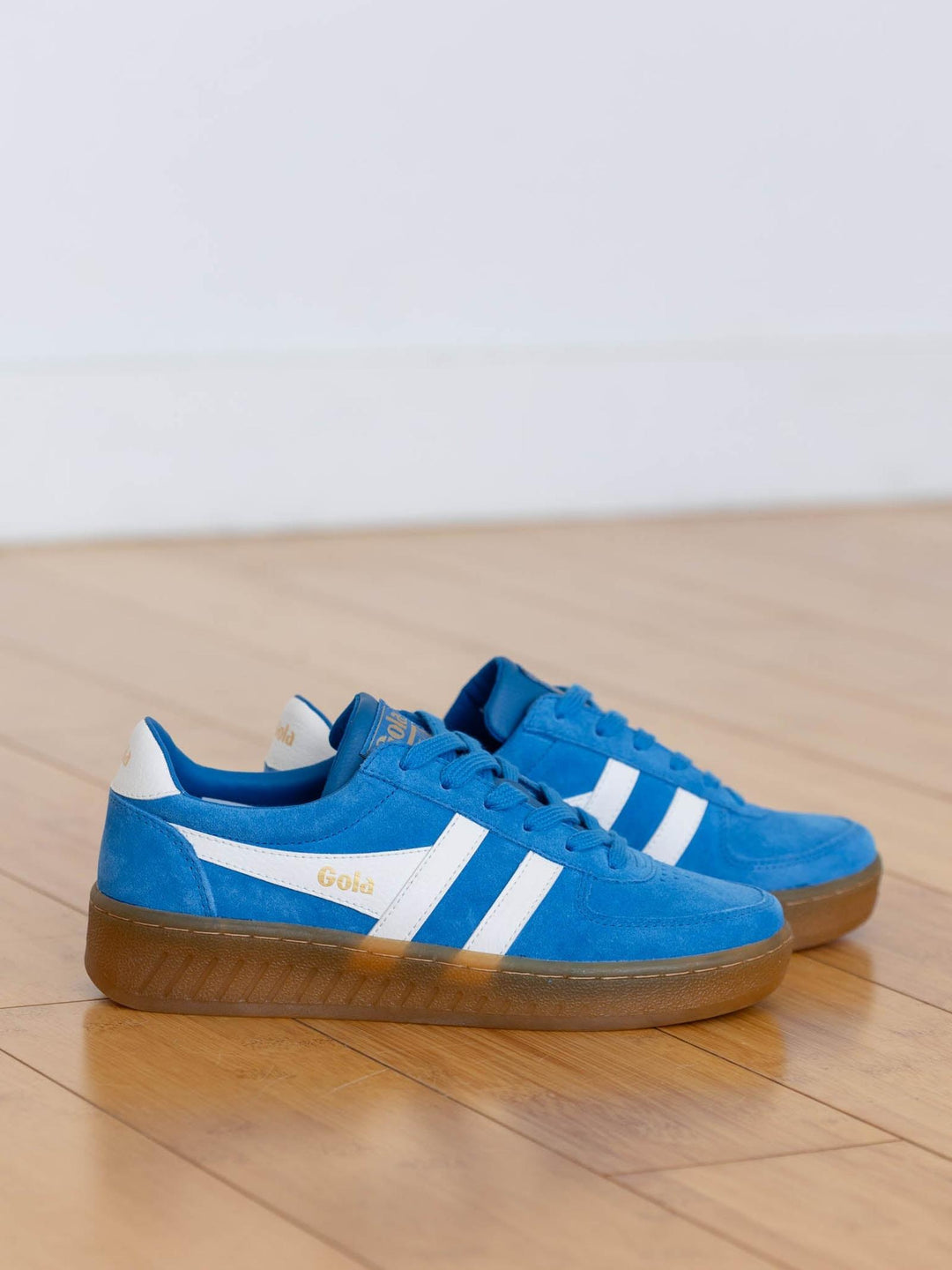 Pair of blue sneakers with white stripes on a wooden floor.
