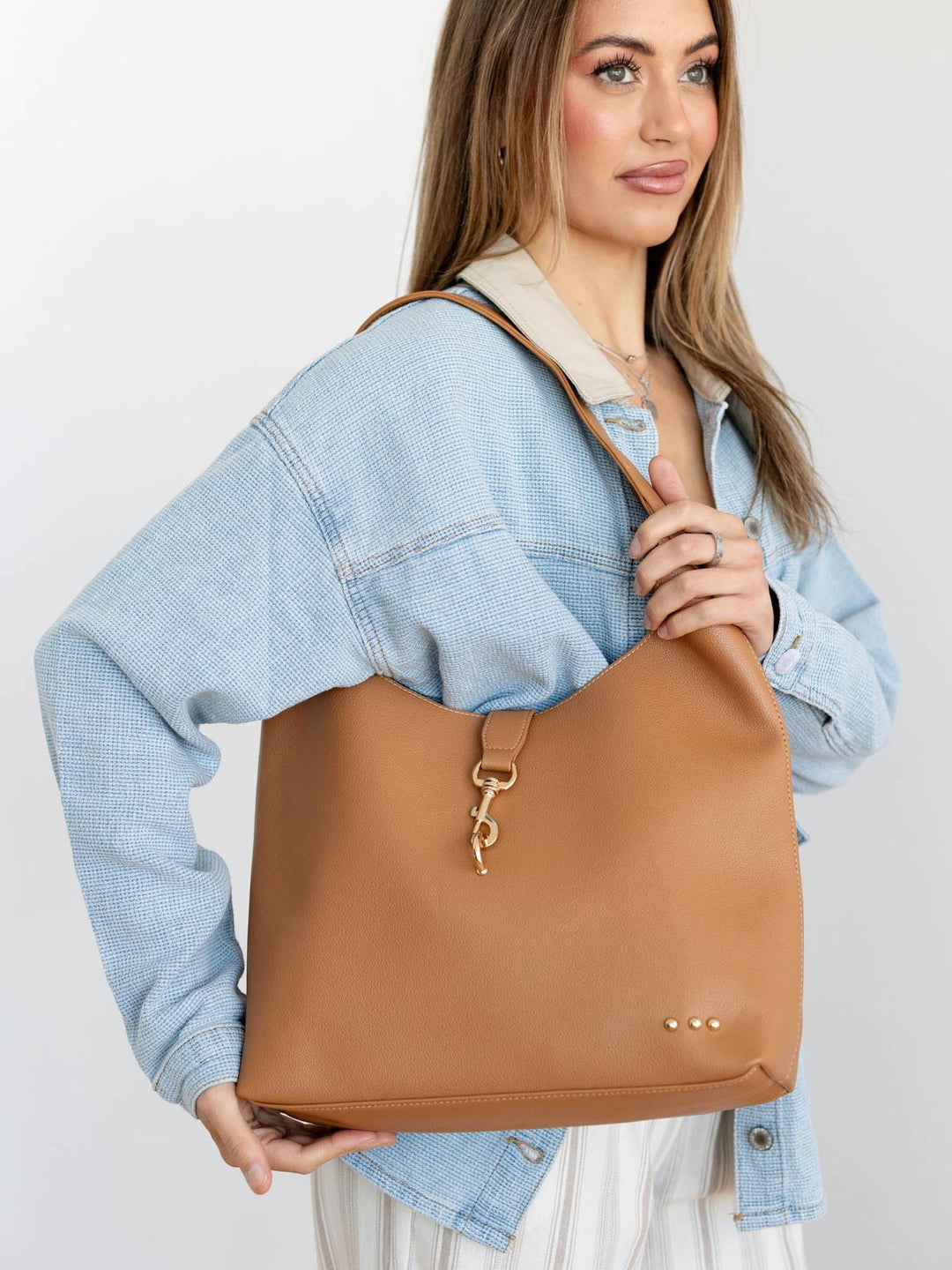 Woman holding a tan leather bag against a plain background
