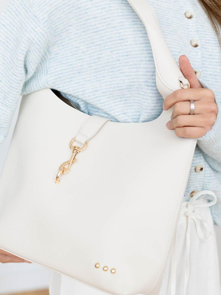 Close-up of a person holding a white handbag with a gold clasp, wearing a light blue sweater.