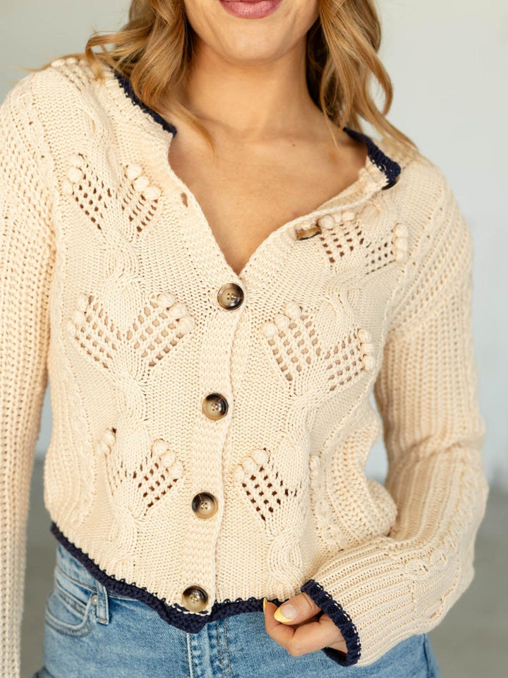 Beige knitted cardigan with button details worn by a person against a neutral background