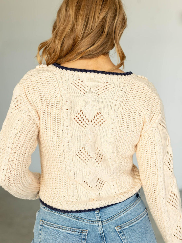 Person wearing a beige knitted cardigan with a subtle pattern, standing against a plain background.