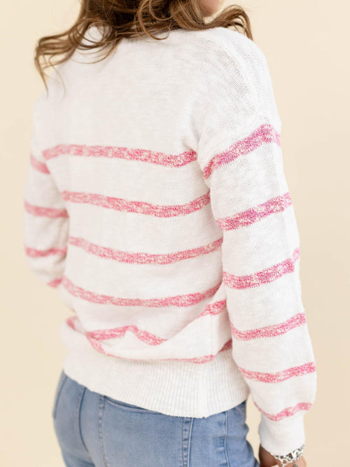 White sweater with pink stripes worn by a person on a beige background