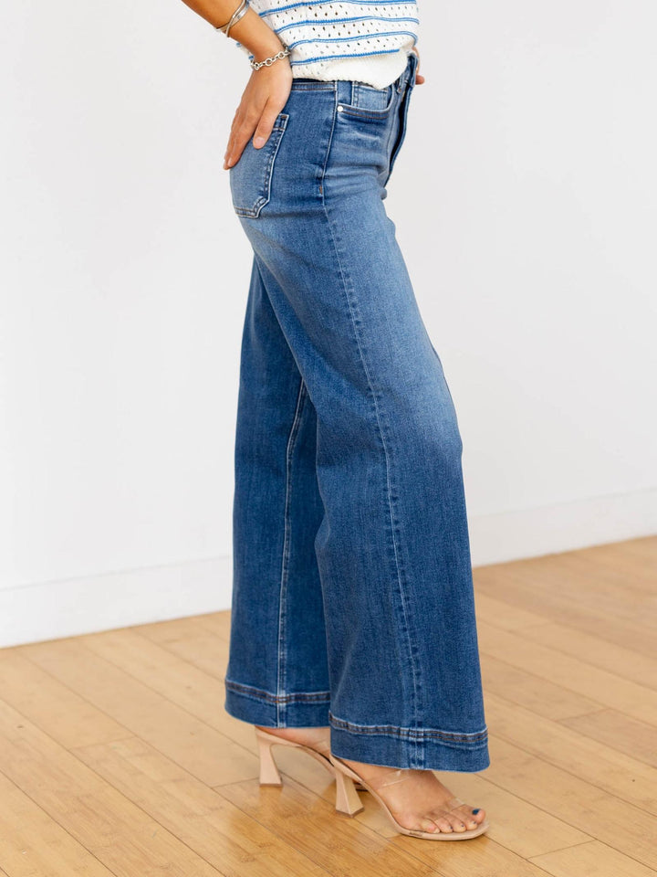 Person wearing blue jeans on a wooden floor with a white wall background