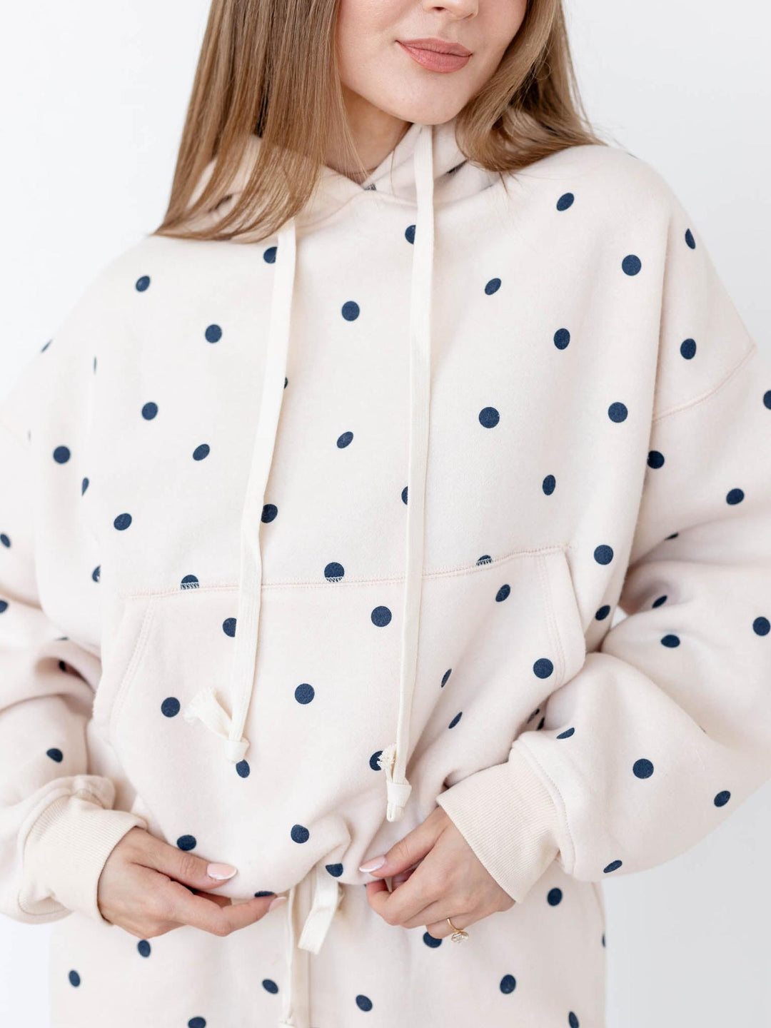 Person wearing a cream hoodie with navy polka dots on a white background