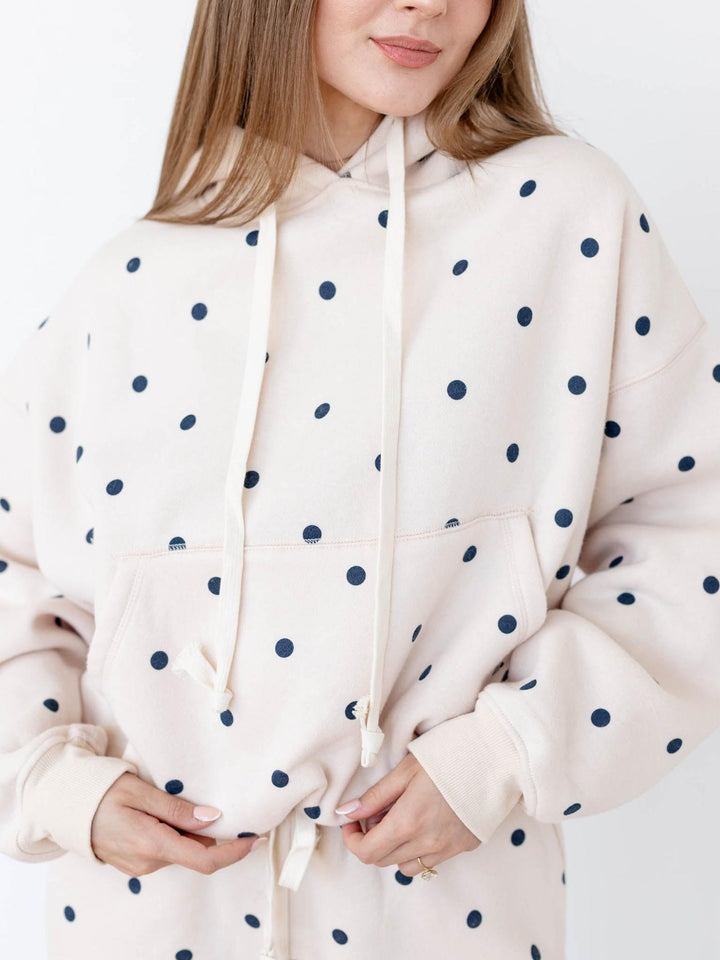 Person wearing a cream hoodie with navy polka dots on a white background