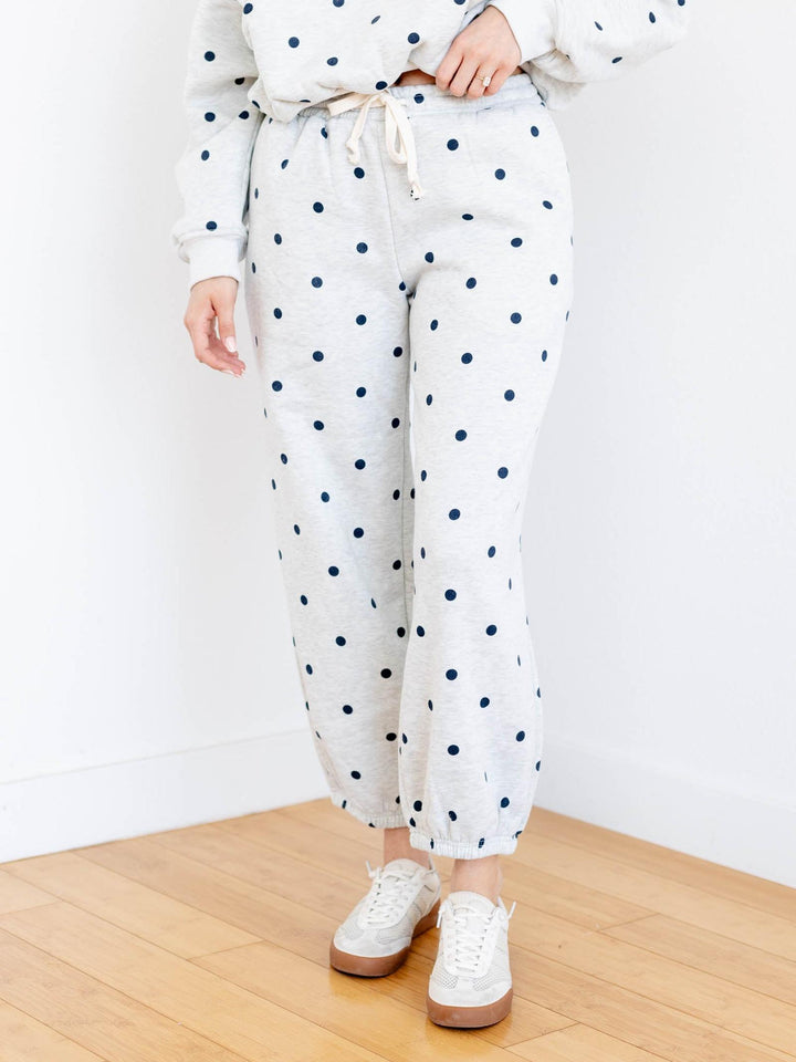 Person wearing white polka dot pants with a white top on a wooden floor.