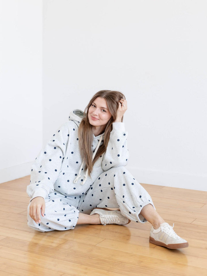 Woman wearing a polka dot onesie sitting on a wooden floor.