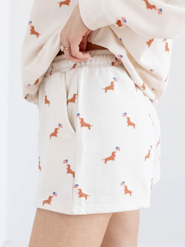 White shorts with dachshund pattern held by a person on a white background